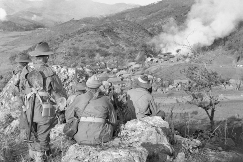 Image: Australian War Memorial | Soldiers from C Company 3RAR watch for the enemy while a village in valley below burns.