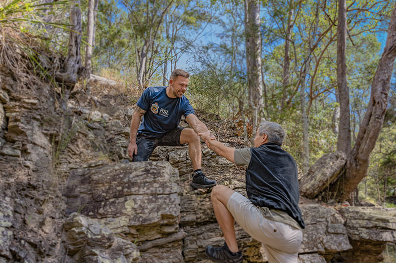 Person helping another up a steep rock on a walking trail. 